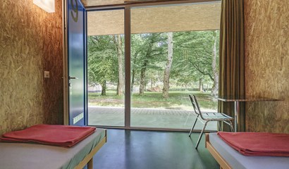 Zwei Betten in einem Zimmer mit Ausblick auf die Zeltwiese.